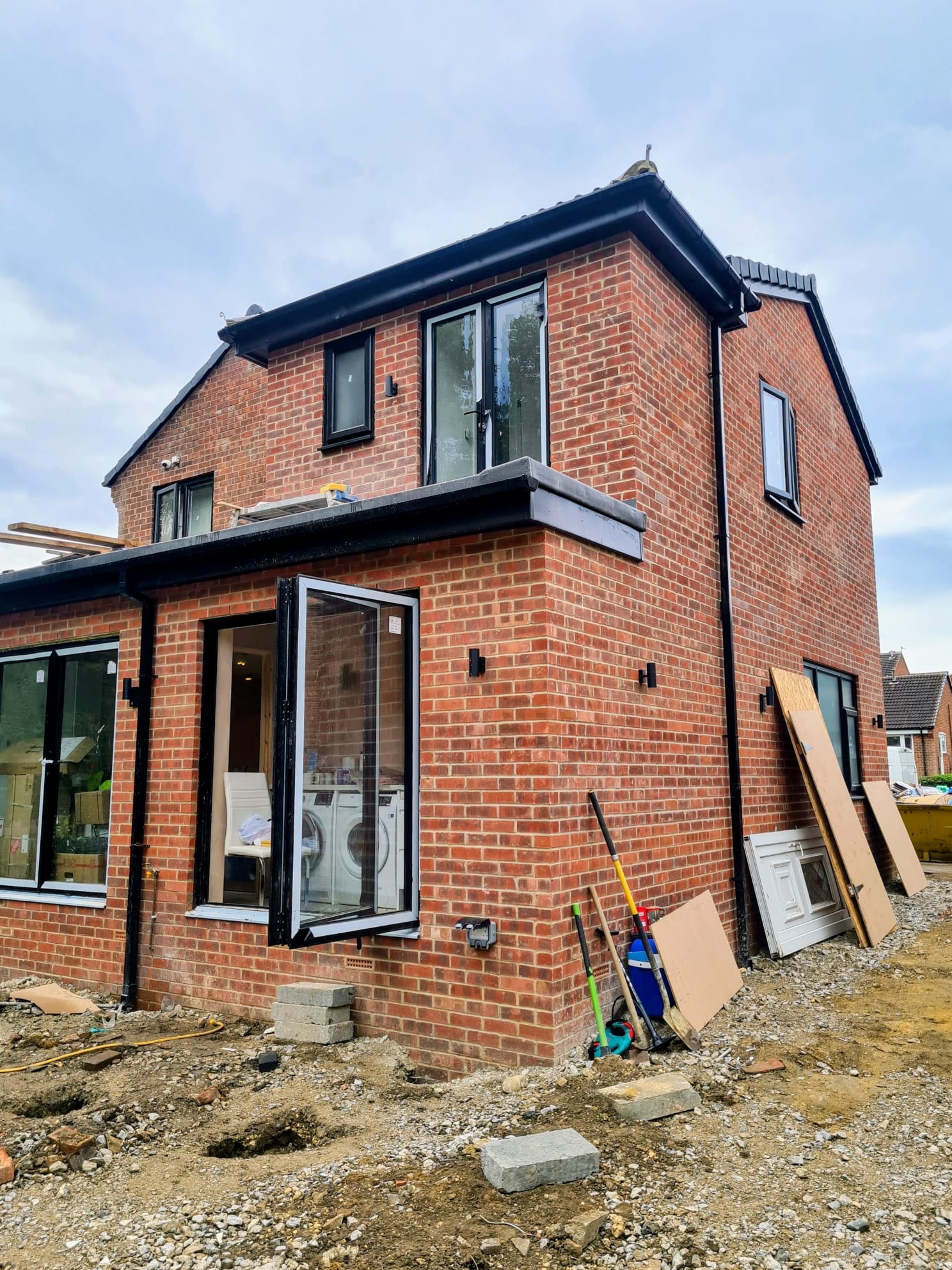 Two-storey side extension under construction with exposed red brickwork and scaffolding, Leeds
